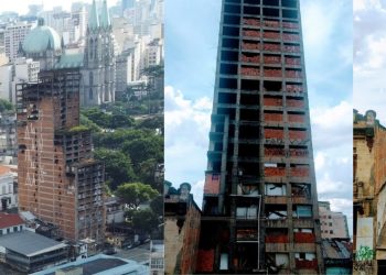 Uma imagem em preto e branco do "Caveirão", um prédio abandonado no centro de São Paulo, com tapumes e pichações. O prédio está cercado por outros edifícios e o céu está nublado. Jornal 25 News, o Jornal do centro de São Paulo.